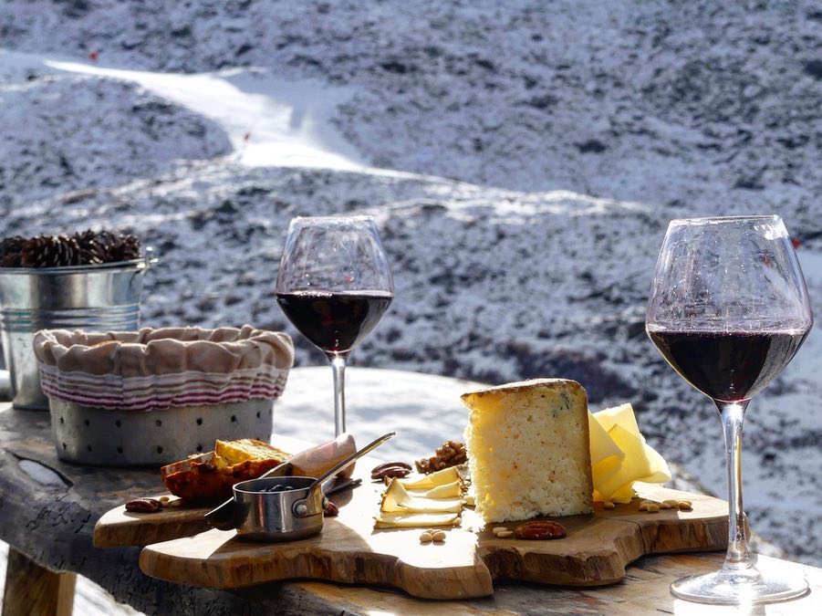 Red wine and cheese board at 'Chez Pépé Nicholas' restaurant in Les Menuires with mountain background